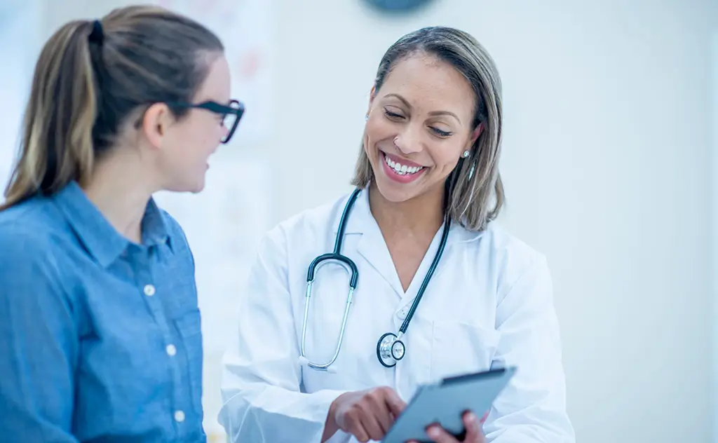 A female doctor converses with a patient in a clinical setting, discussing health concerns and treatment options.